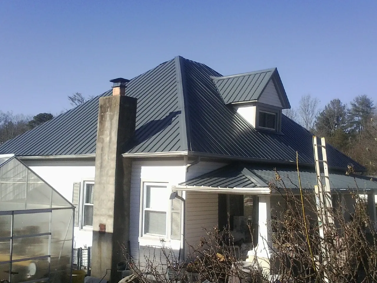 Dark blue standing seam metal roof on a white farmhouse with dormer — Slate & Tile Roof Repair by Roofing Brothers in Oak View