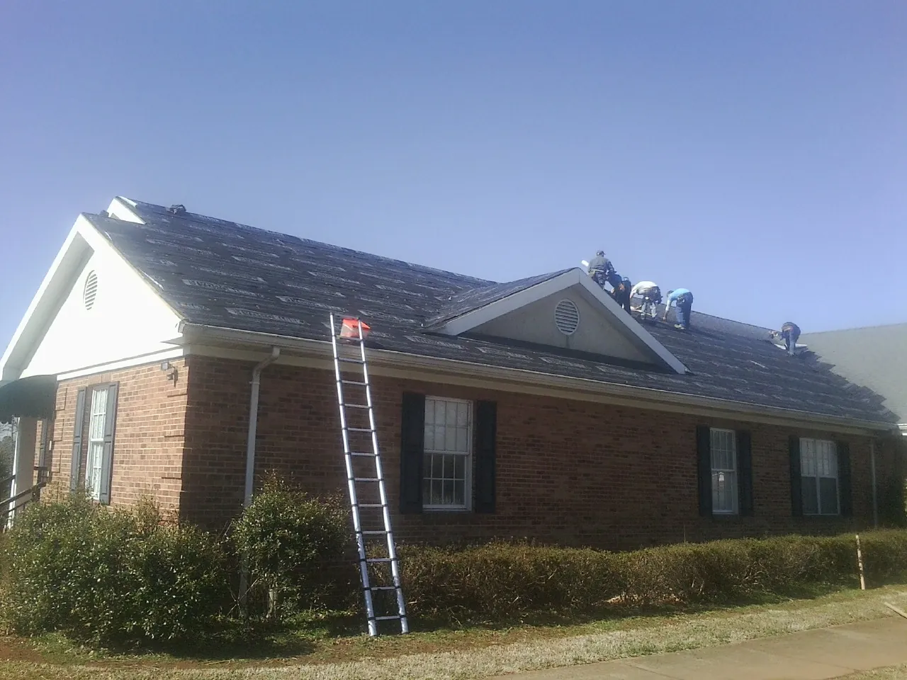 Crew tearing shingles off a brick ranch roof with a ladder set — Emergency Roof Repair work by our crew in Oak View